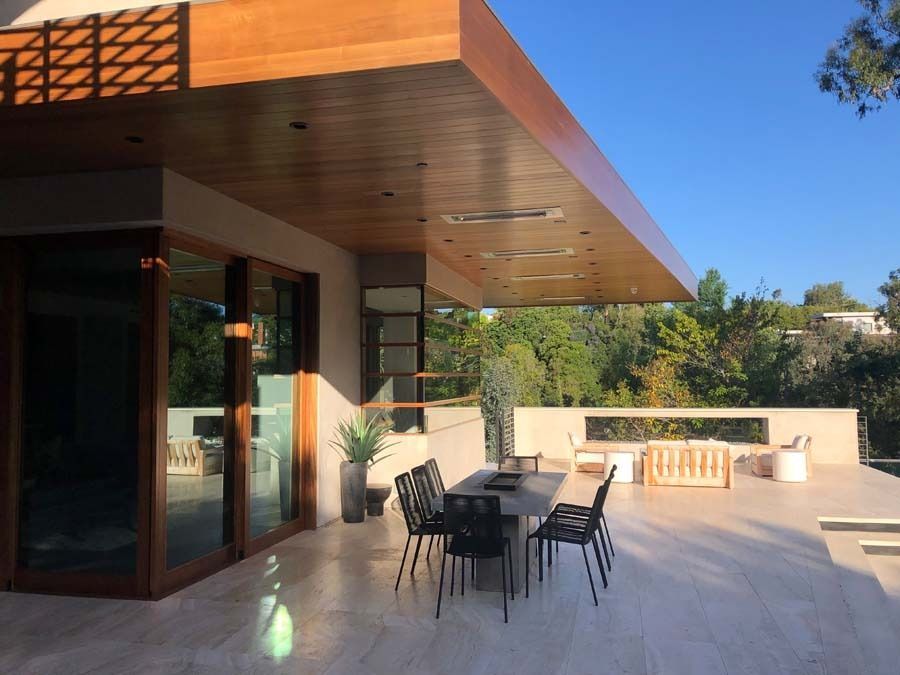 Outdoor patio with wooden ceiling, dining table, and chairs overlooking a lush green hillside.