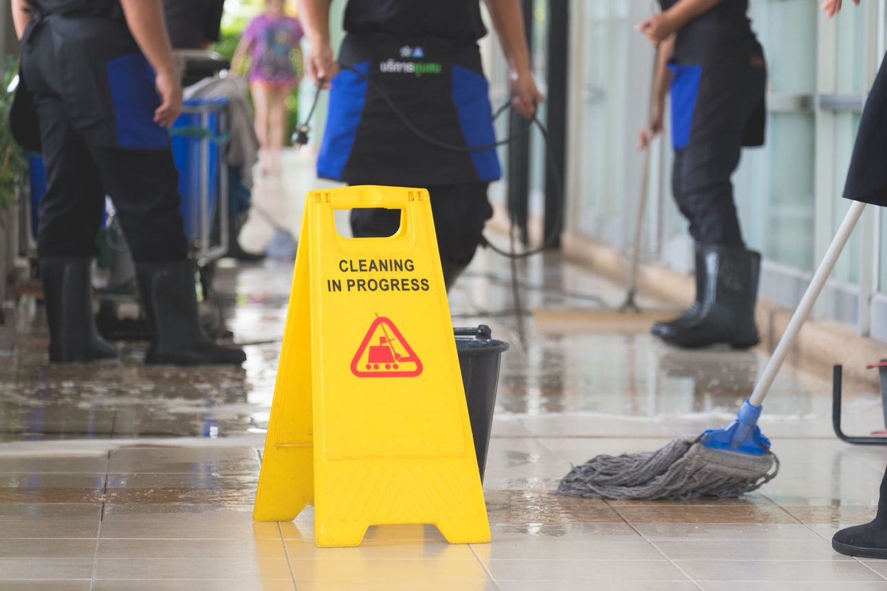 Yellow wet-floor caution sign in a lobby while cleaners mop the wet floor around it