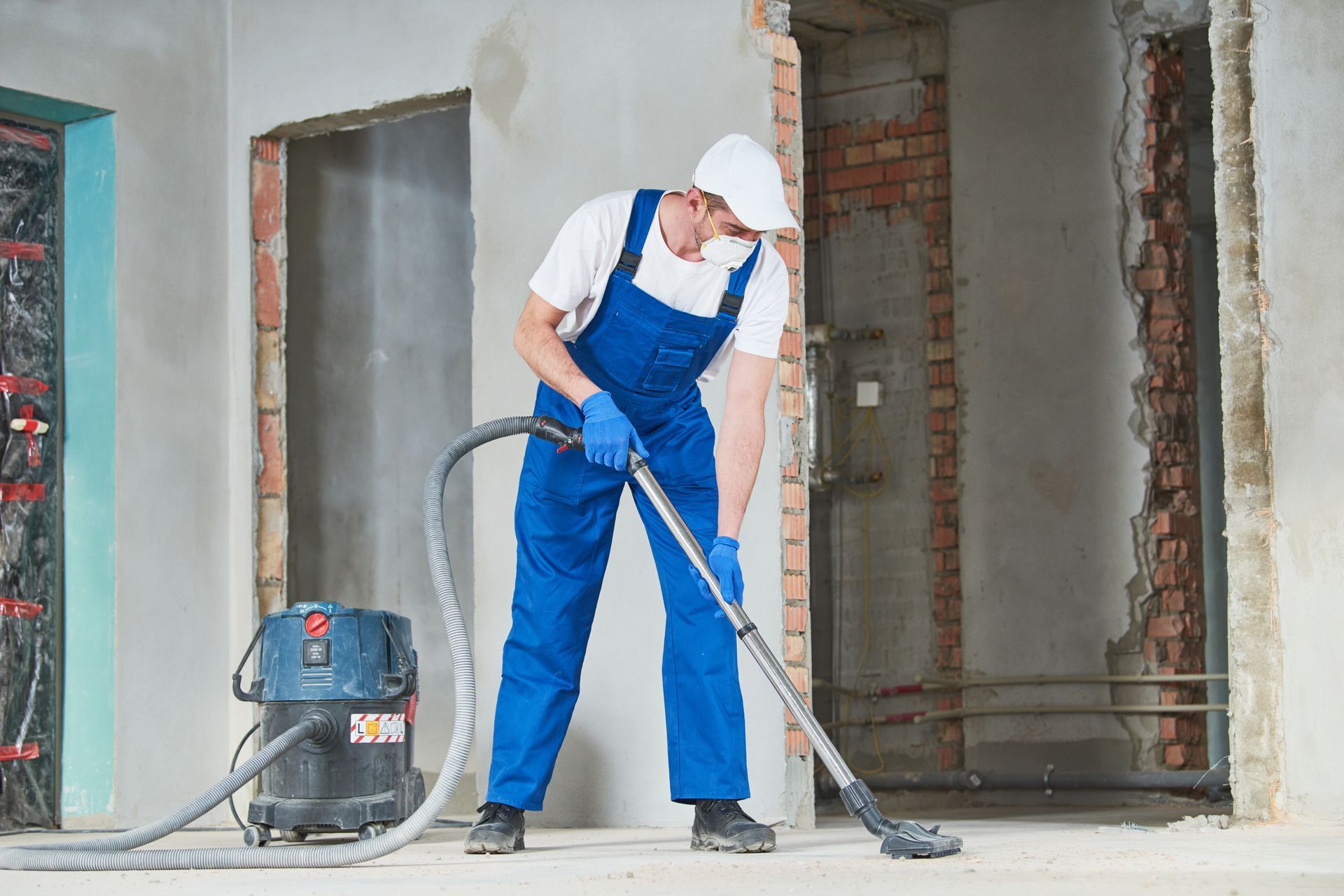 Worker in blue overalls using a floor grinder at a construction site interior
