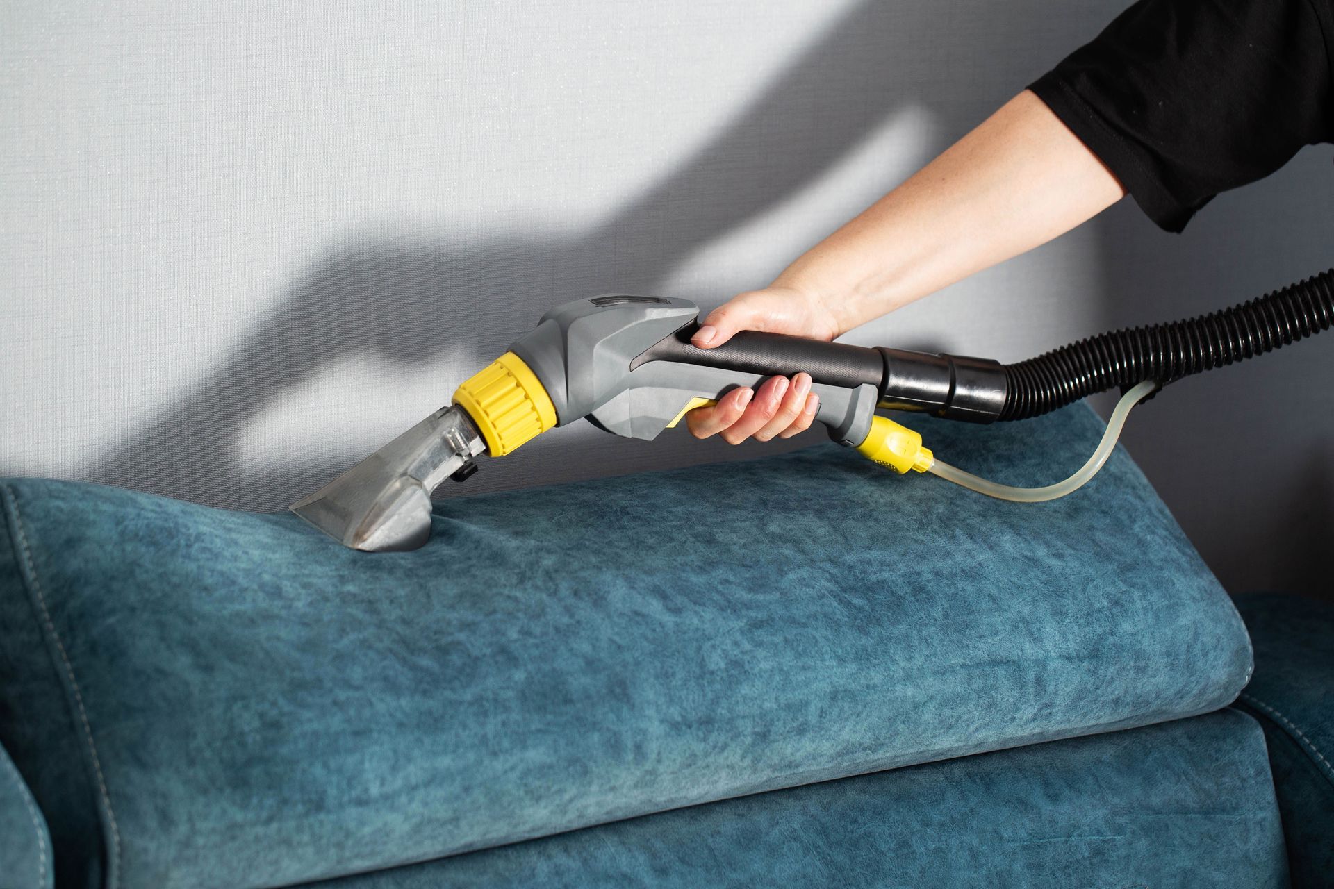 Hand vacuum cleaning a blue sofa cushion with a flexible hose