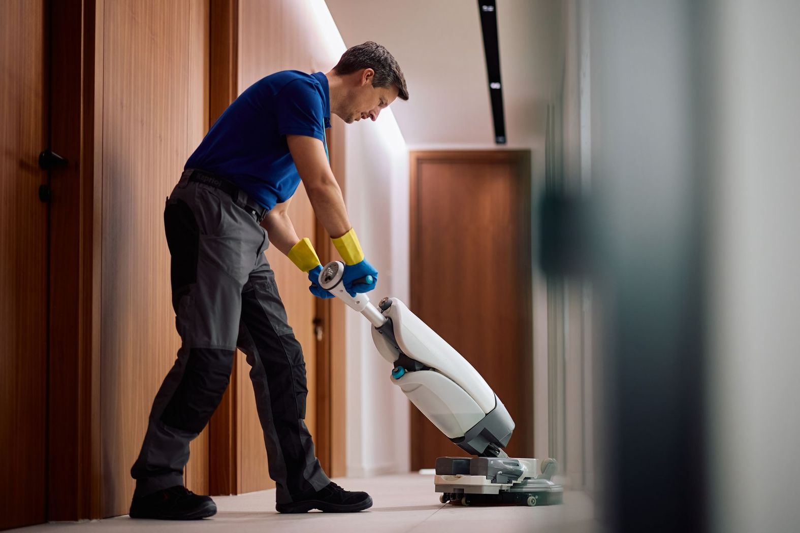 Person vacuuming a hallway floor with a white upright vacuum cleaner