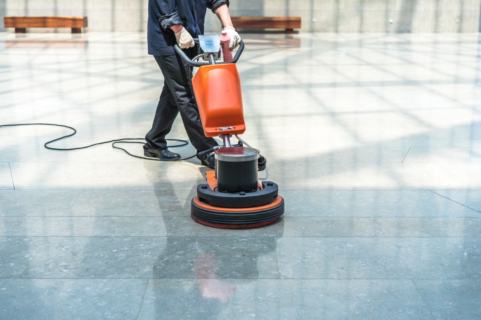 Person using an orange floor buffer on a shiny tiled floor indoors