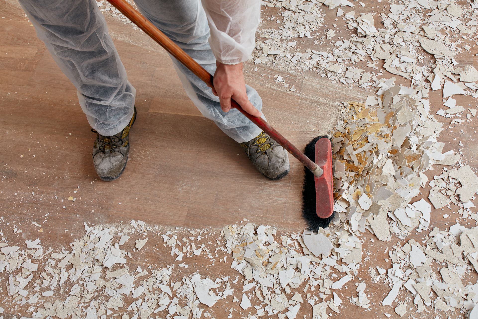 Worker sweeping debris from a floor with a push broom and dustpan