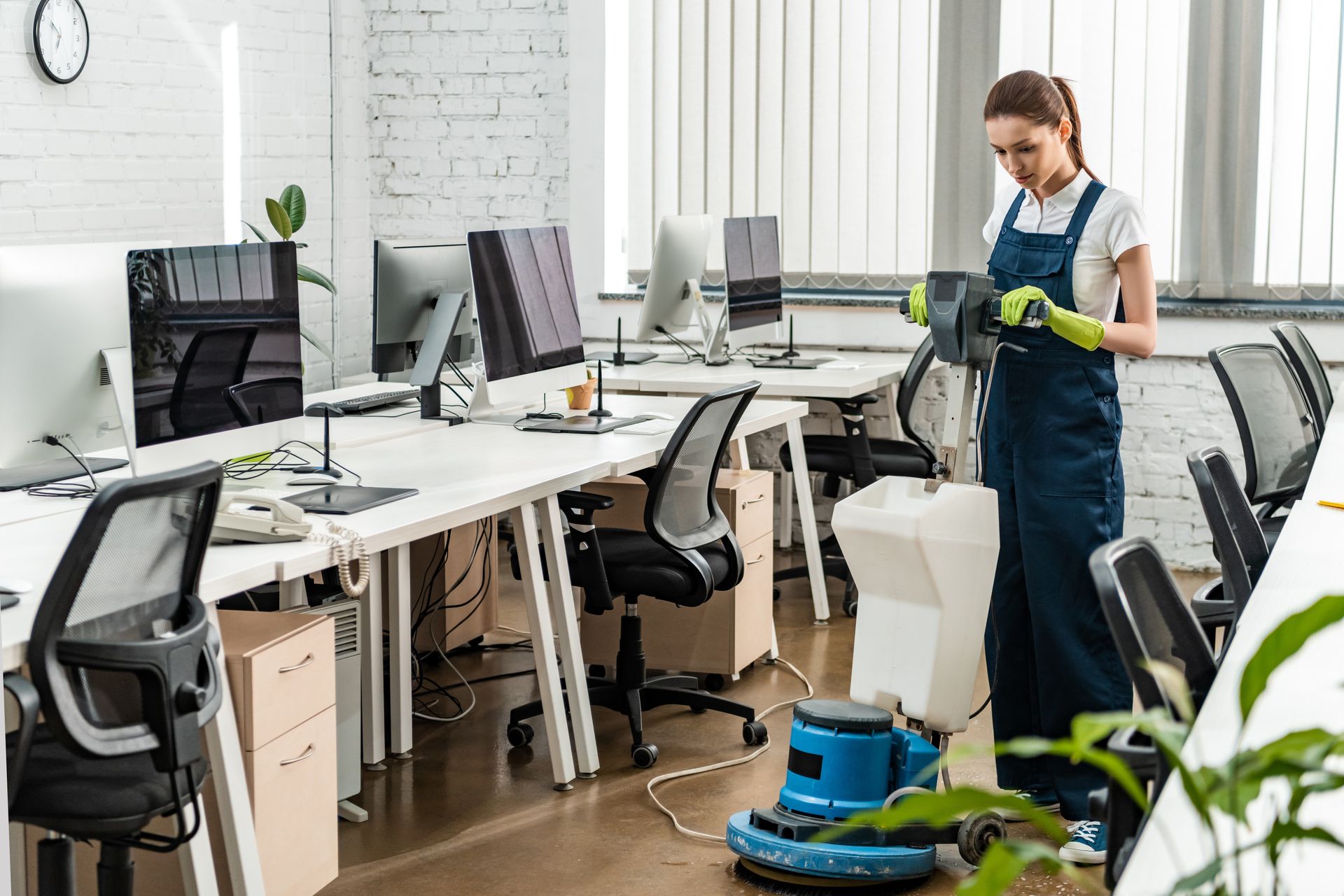 Cleaner vacuuming office floor beside desks and computers