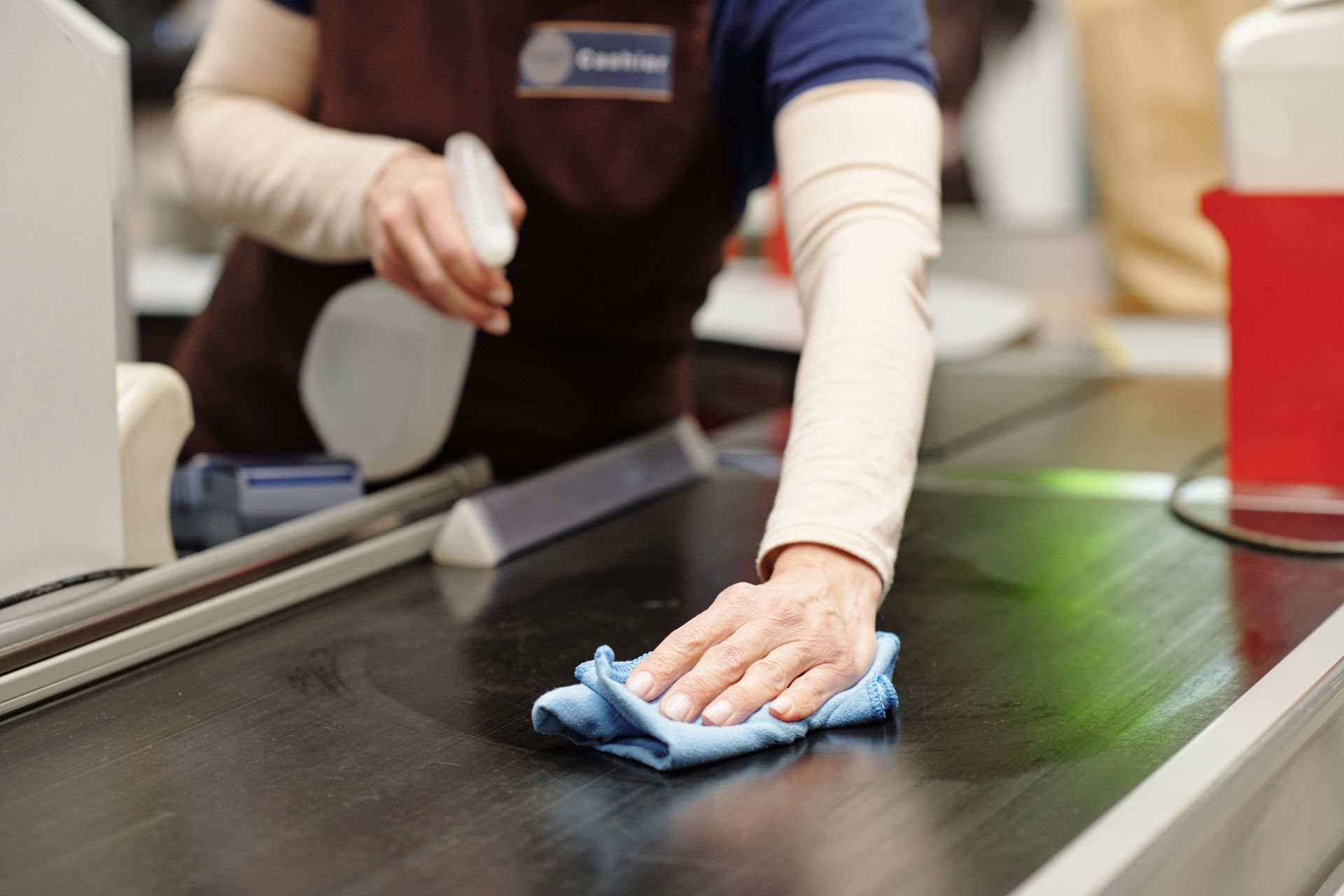 Person wiping a supermarket checkout conveyor with a blue cloth