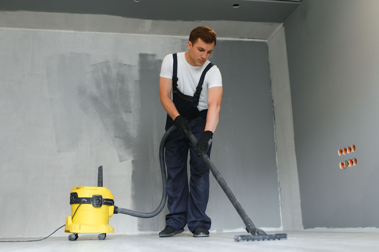 Man vacuuming a room with a yellow wet-dry vacuum and hose