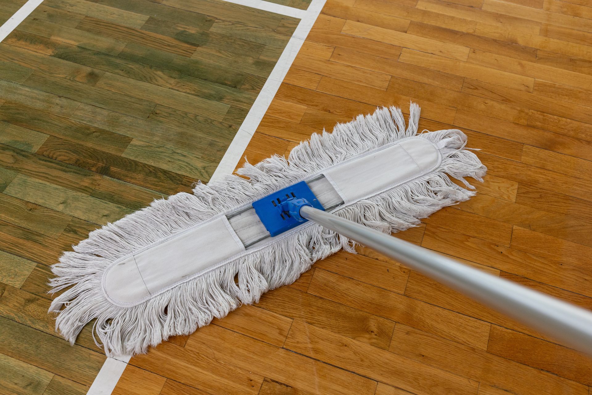 White mop cleaning a wooden gym floor with painted court lines