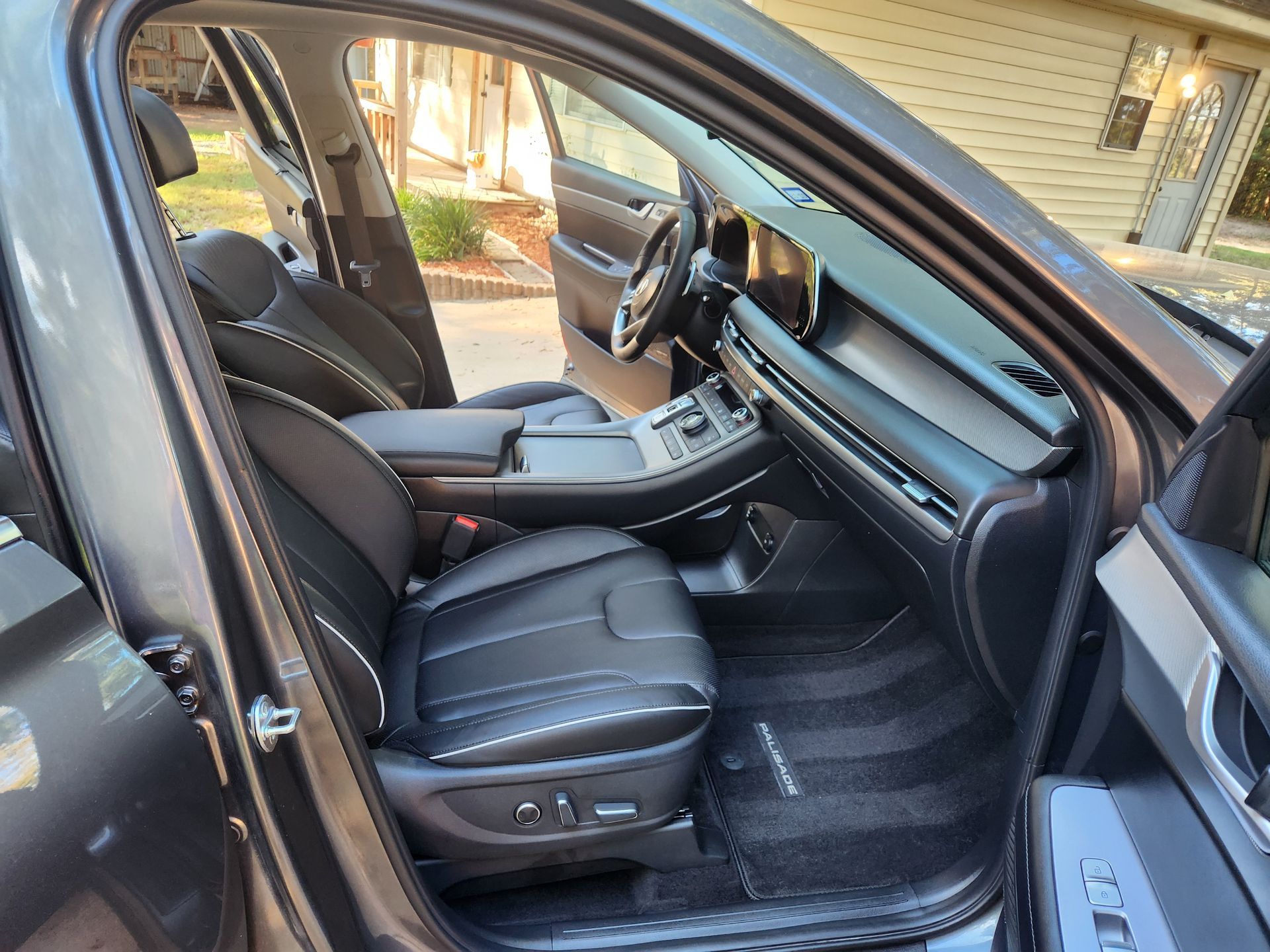 Gray car interior with black leather seats, open driver's door, and floor mats.