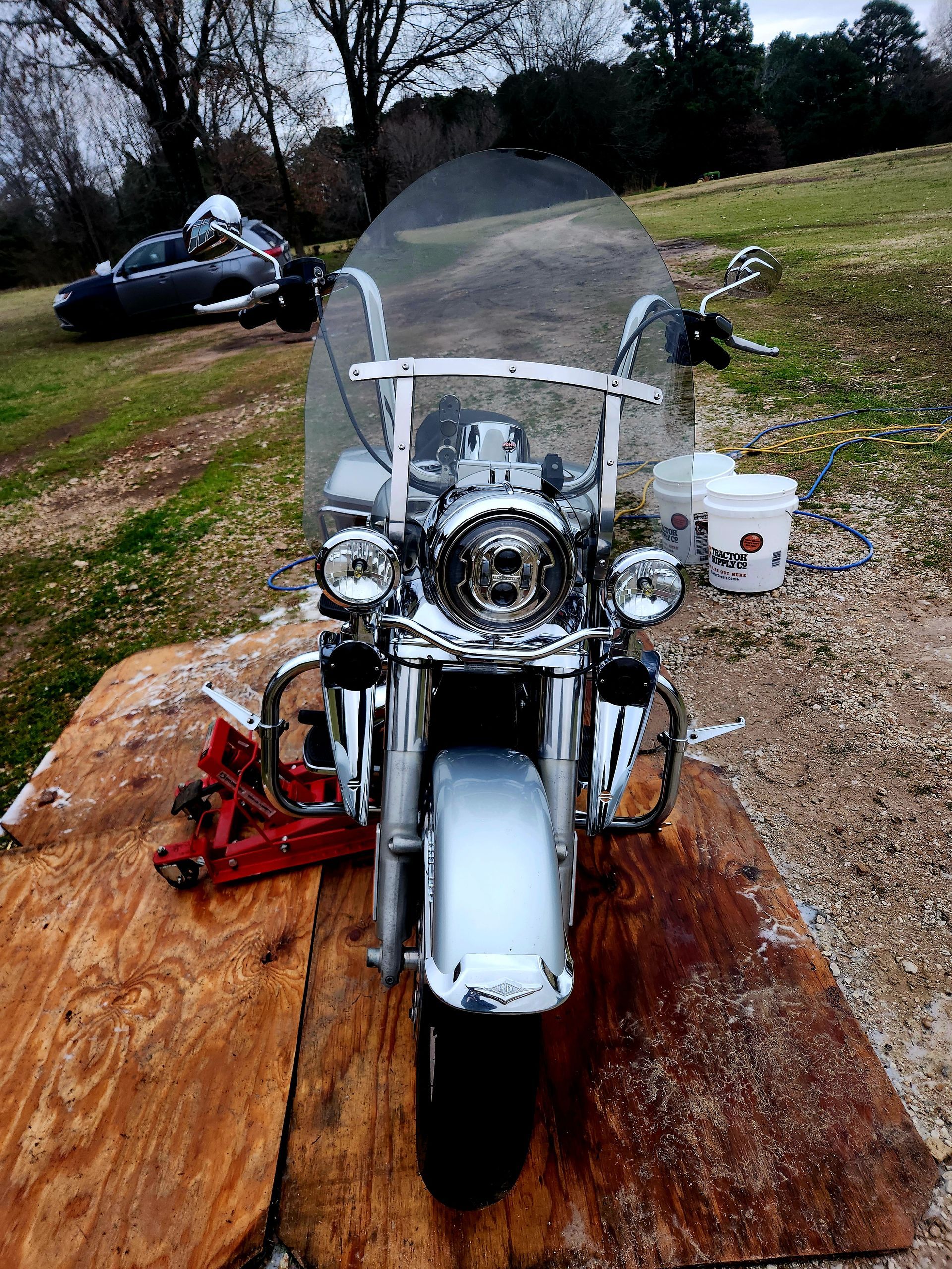 Silver Harley-Davidson motorcycle parked on a wooden board, with a second motorcycle in the background, outdoors.