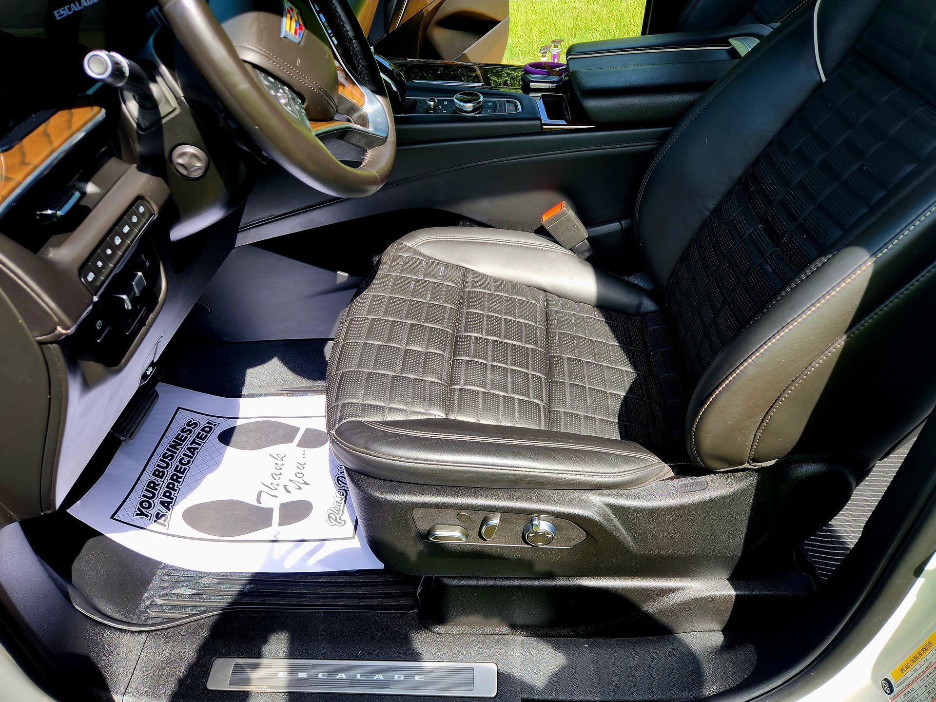 Car interior with black driver’s seat, steering wheel, and open door, sunlight on the floor mat