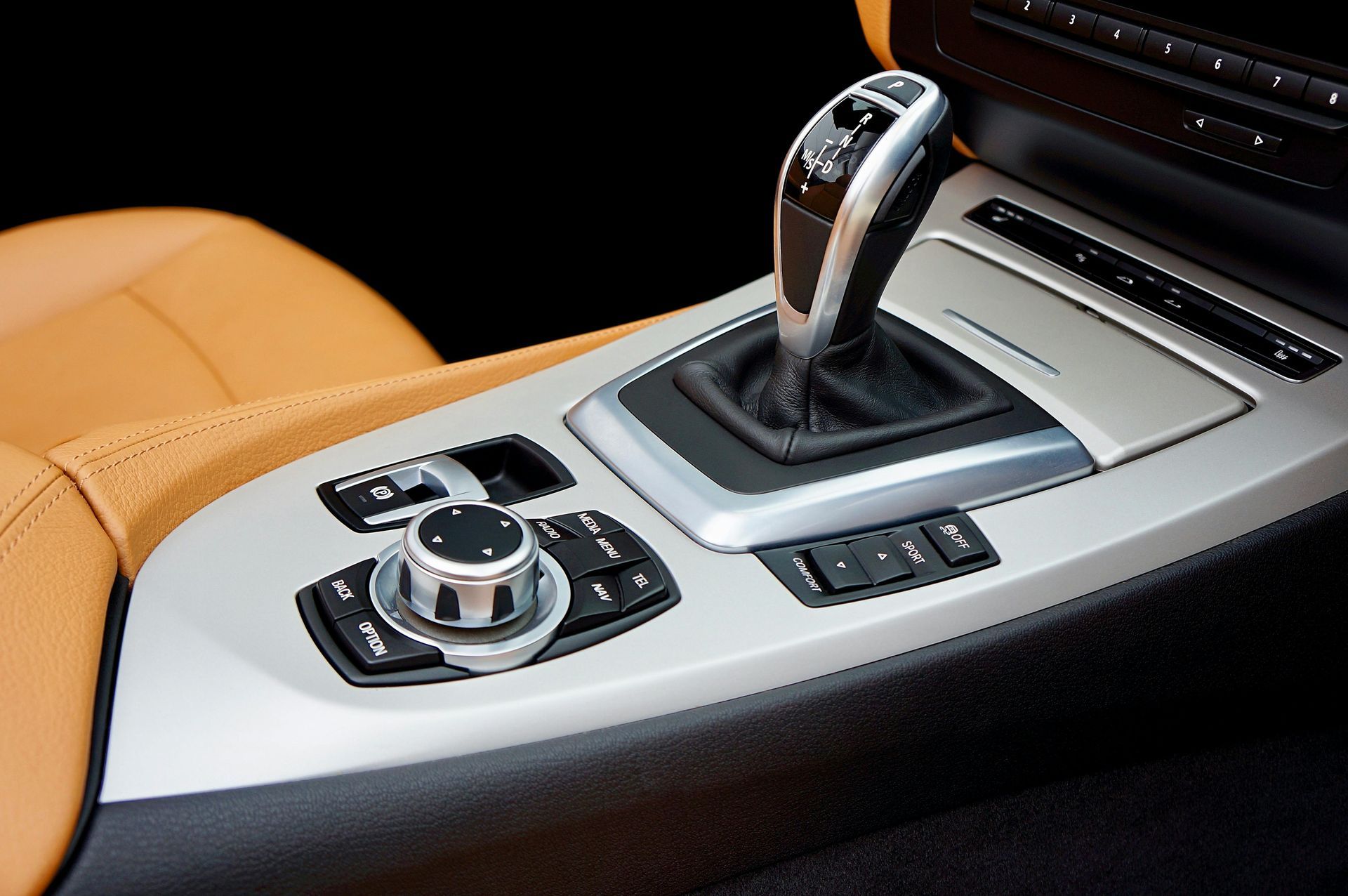 Car's interior with a gear shift, infotainment controls, and tan leather.