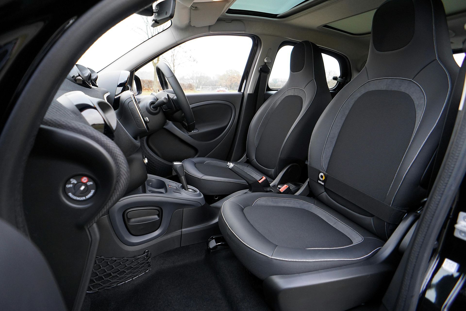 Interior of a small black car with black and gray seats, a steering wheel, and a sunroof.