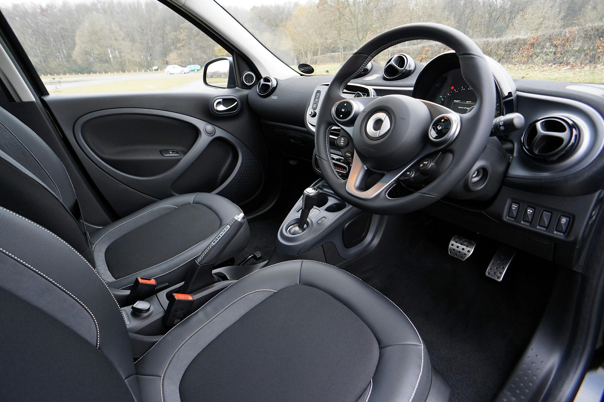 Interior of a Smart car: black and gray seats, steering wheel, dashboard, and gear shift.