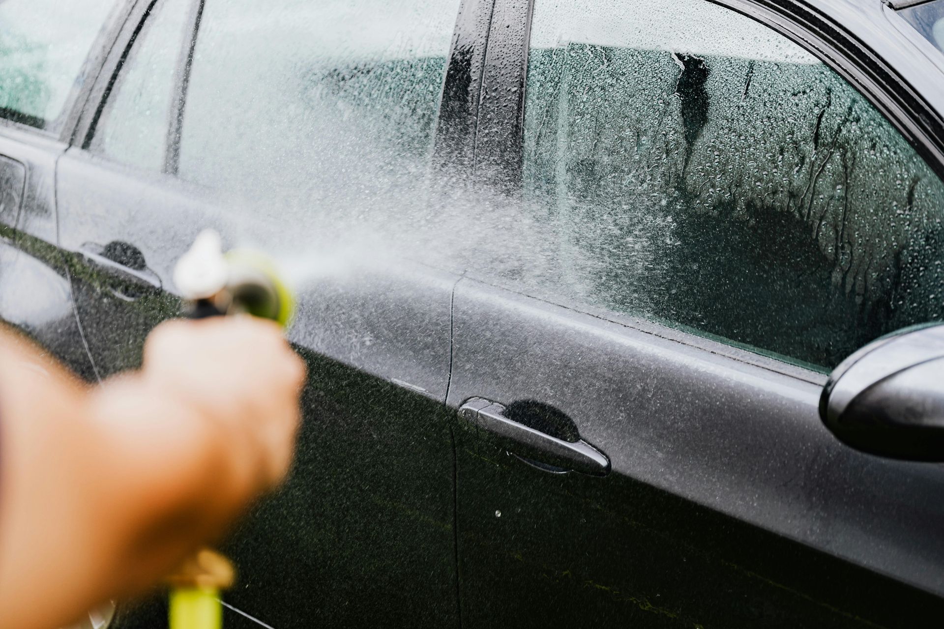 Person washing a black car with a water hose.