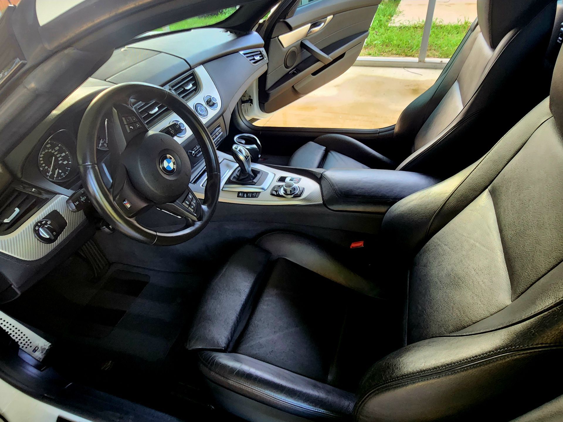 Black BMW interior with leather seats, steering wheel, center console, and open door.