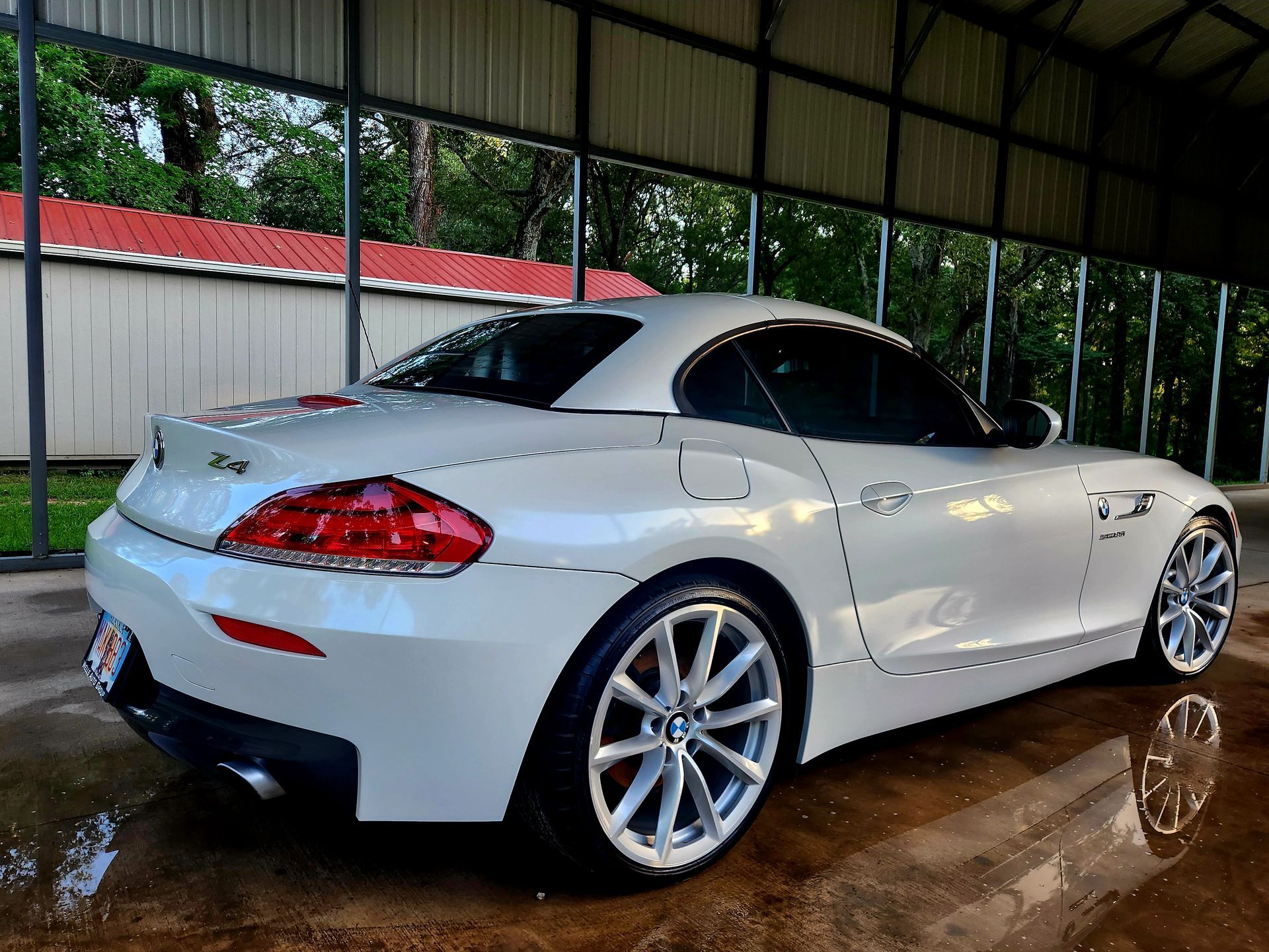 White sports coupe parked indoors on a wet floor under a covered structure, rear three-quarter view