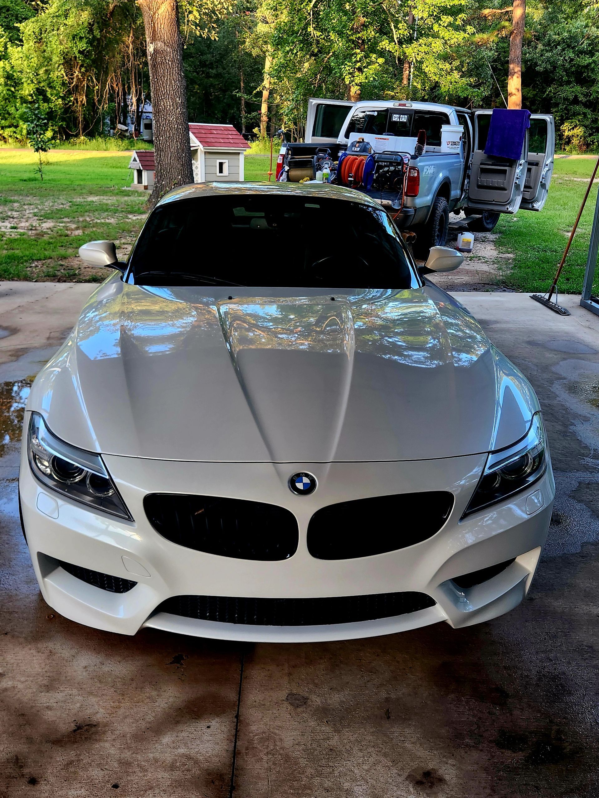 White BMW sedan parked on a driveway with trees and a house in the background