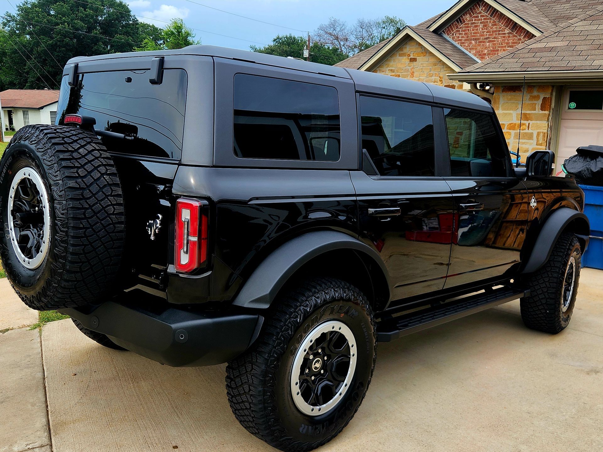 Black SUV with spare tire parked in a driveway in front of a brick house