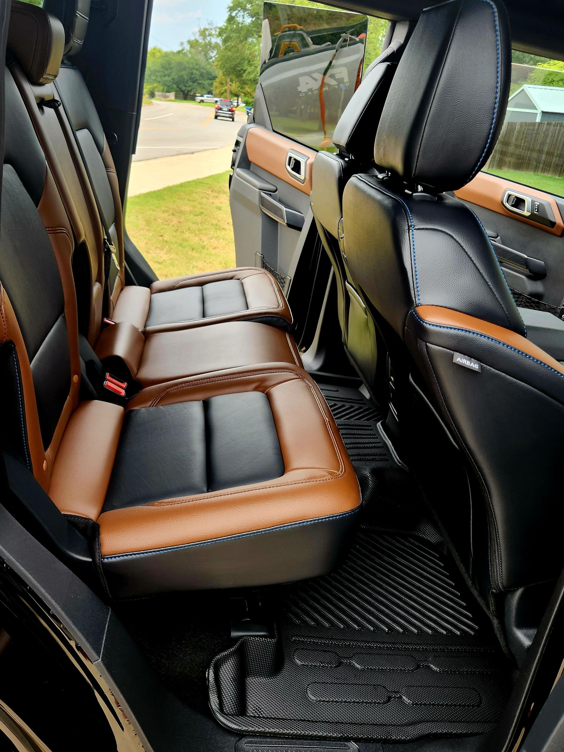 Black and brown leather car interior with rear seats and an open door, showing the outside lawn.