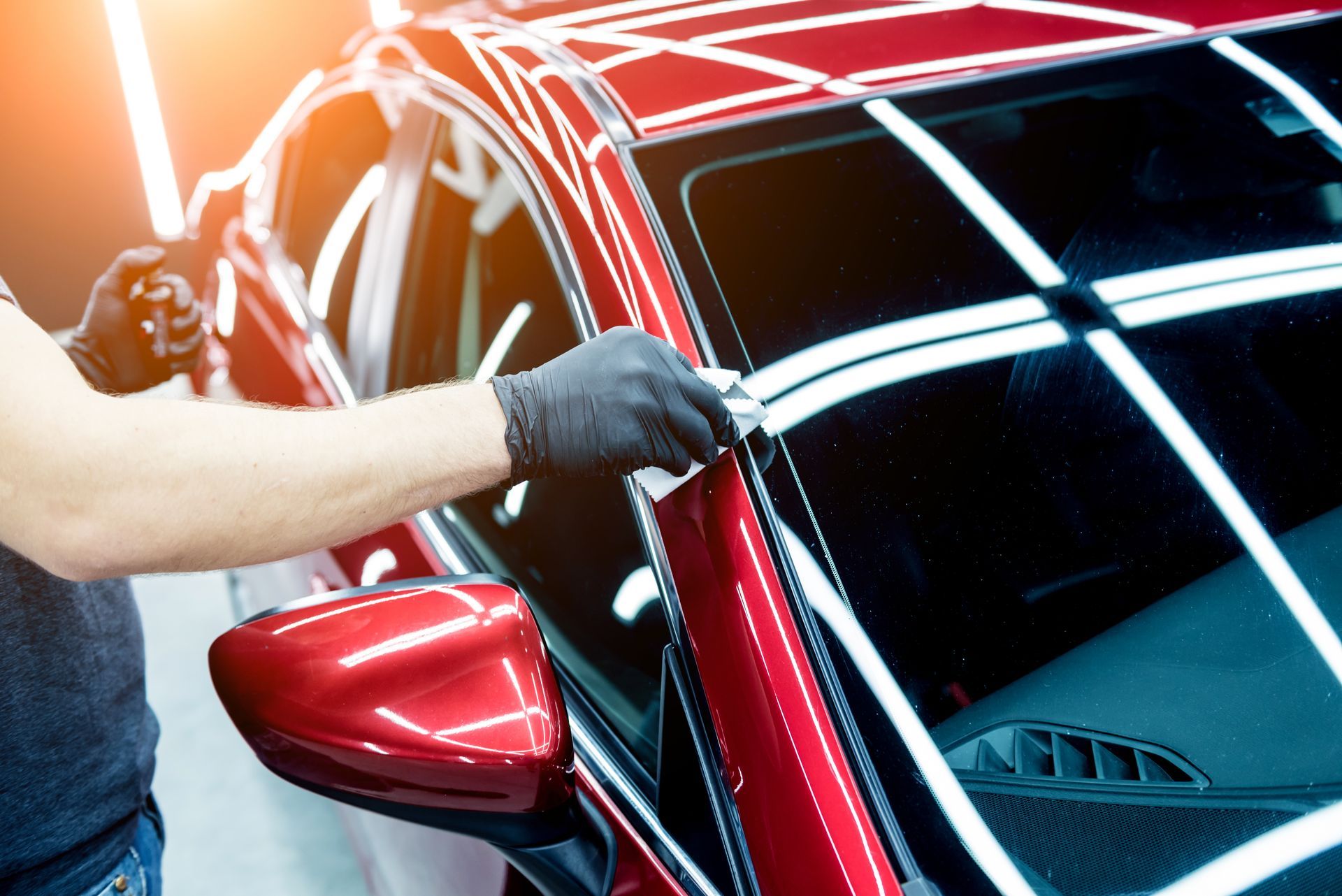 A person wearing gloves applying a ceramic coating to a red car in a well-lit garage.