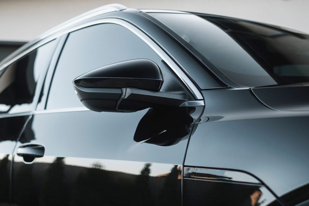 Black car with tinted windows and side mirror, parked outdoors.