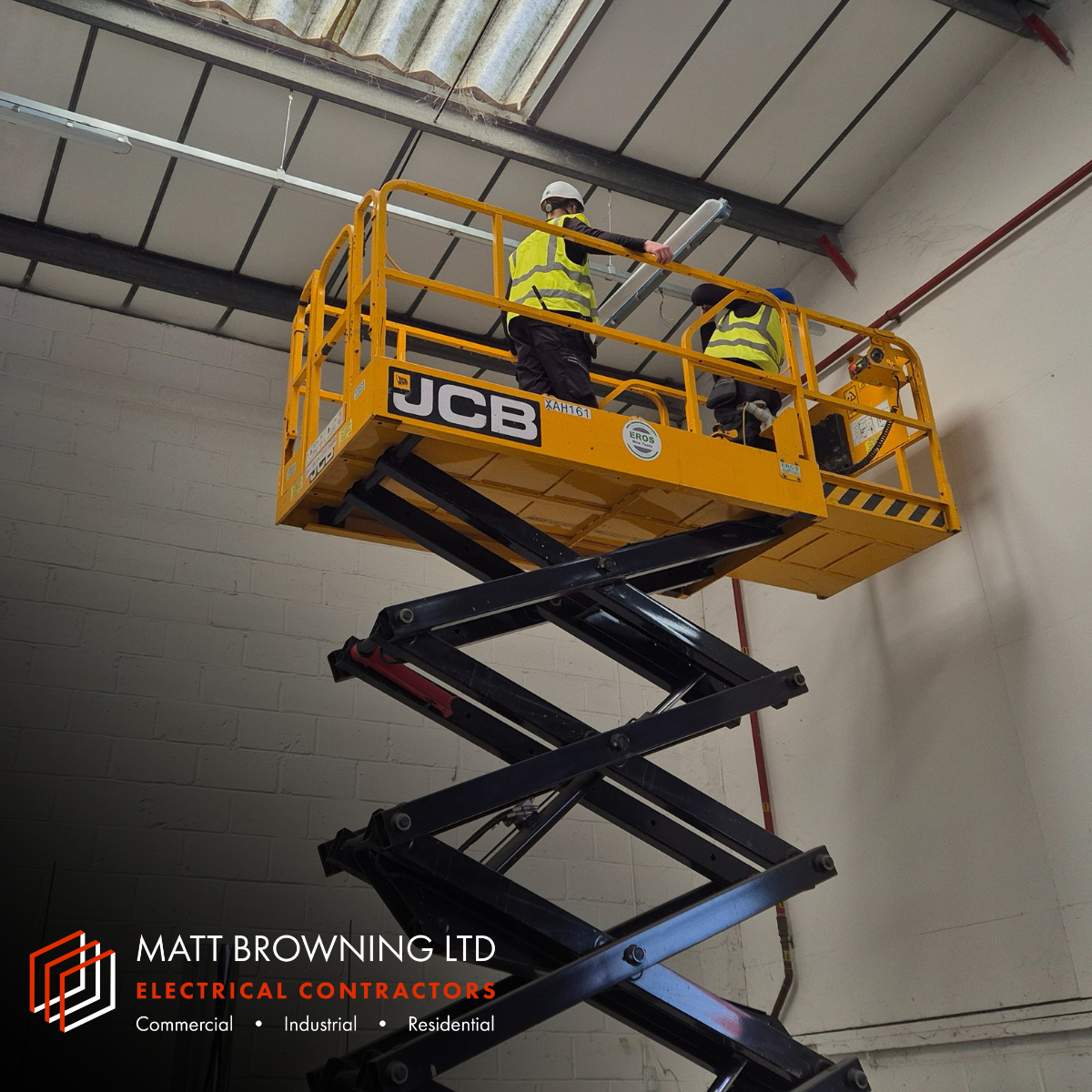 Qualified electrician and electrical apprentice from Matt Browning Electrical Contractors installing energy efficient lighting at high level in a warehouse using a scissor lift in Bracknell near Wokingham.