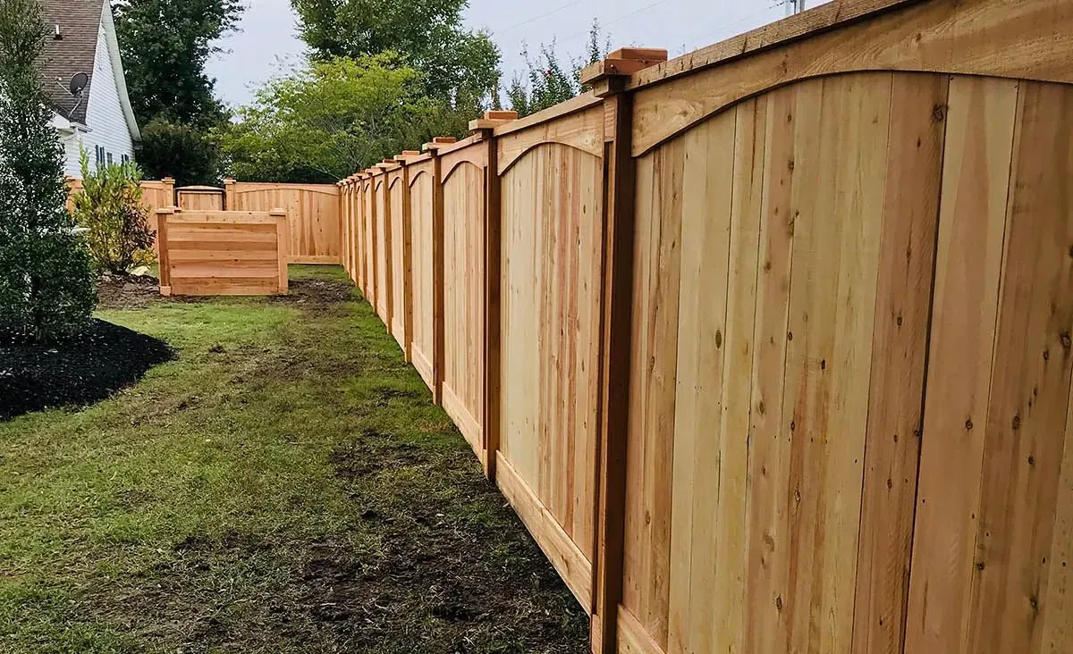 New wooden privacy fence along a grassy backyard with trees and a gate in the distance