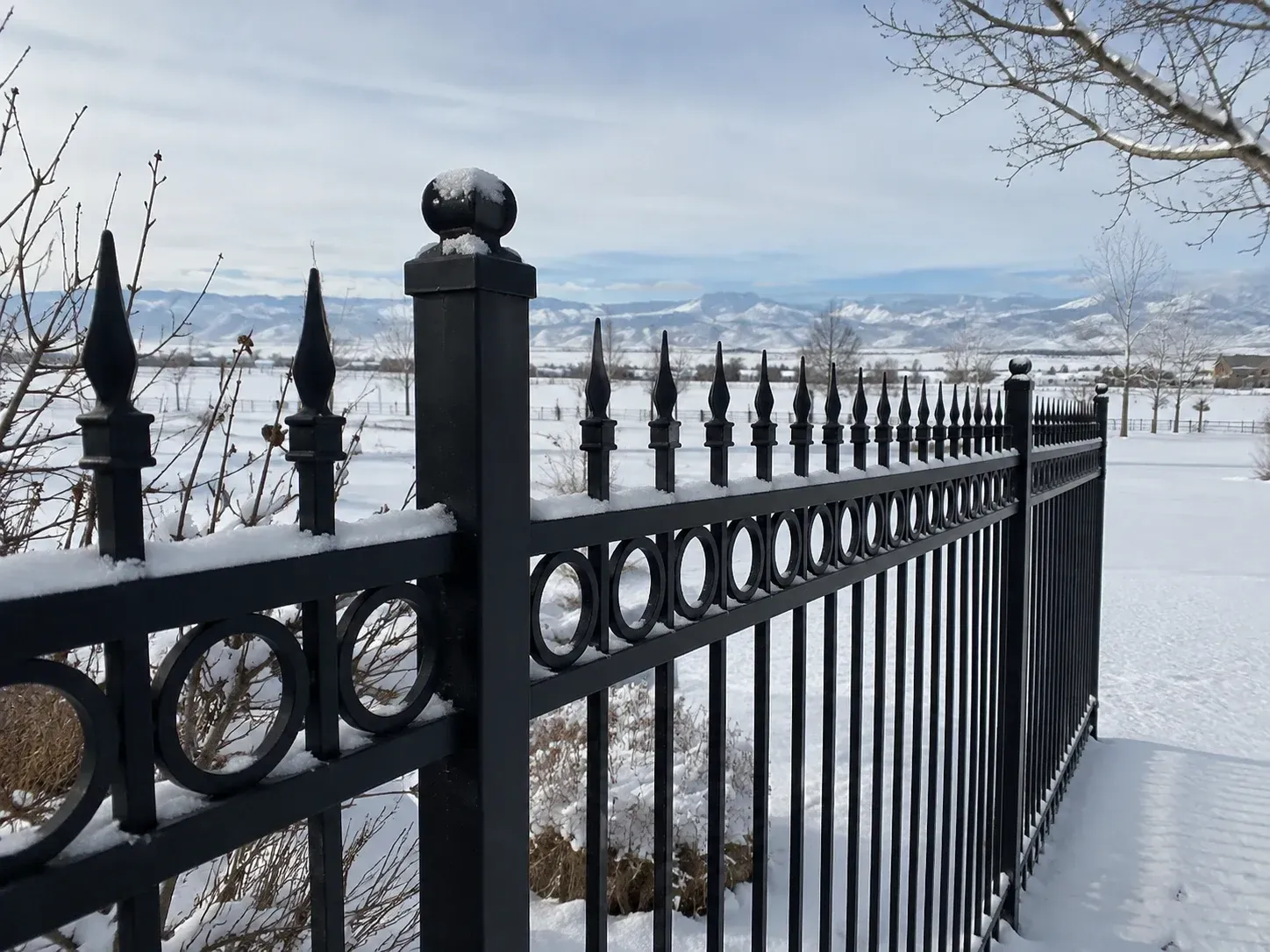 Black iron fence overlooking a snowy landscape and distant mountains under a cloudy sky