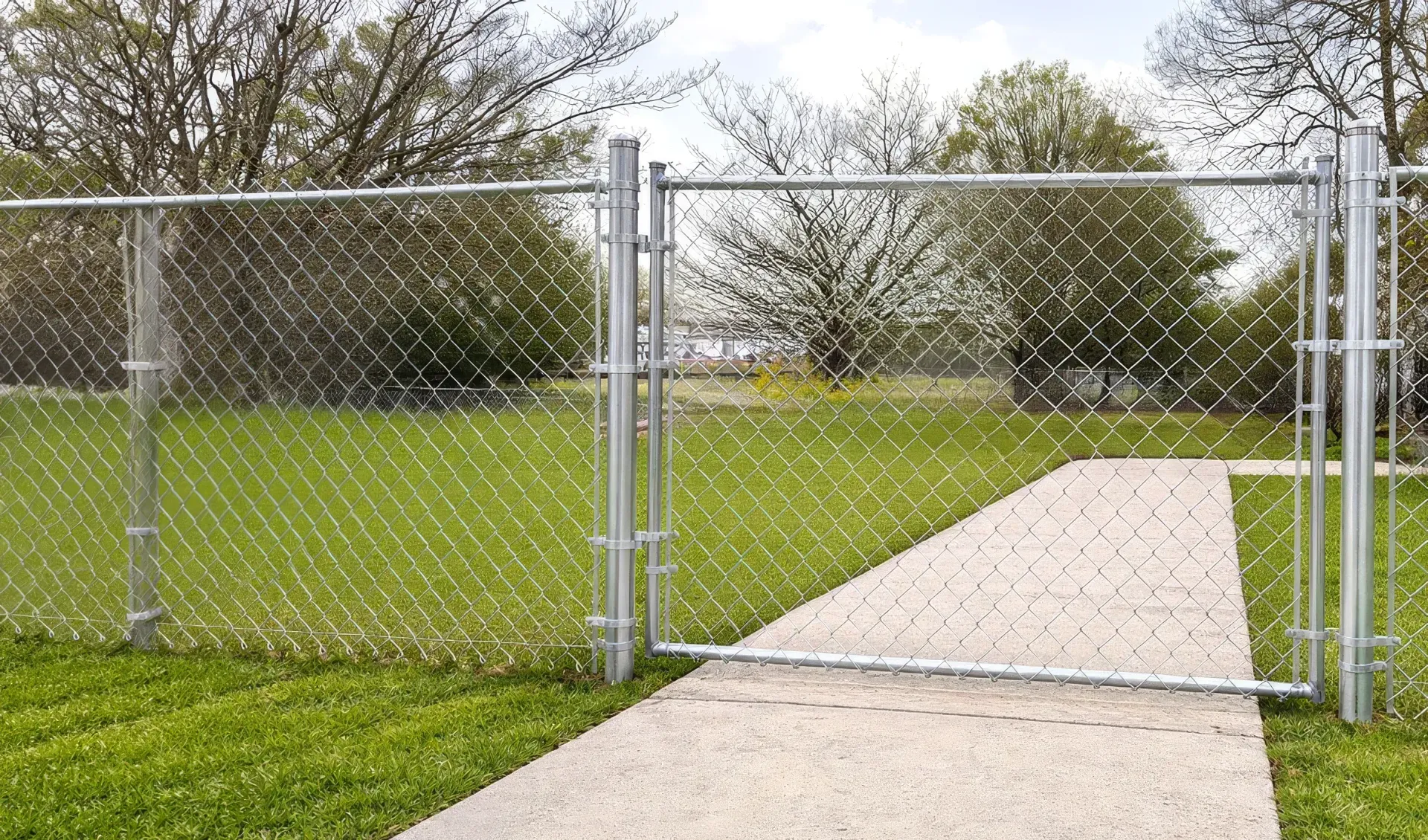 Open chain-link gate beside a concrete path leading into a grassy park