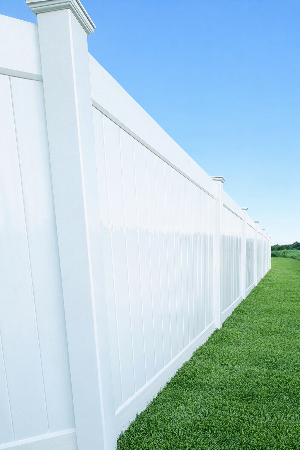 White vinyl fence stretching along a green lawn under a clear blue sky.