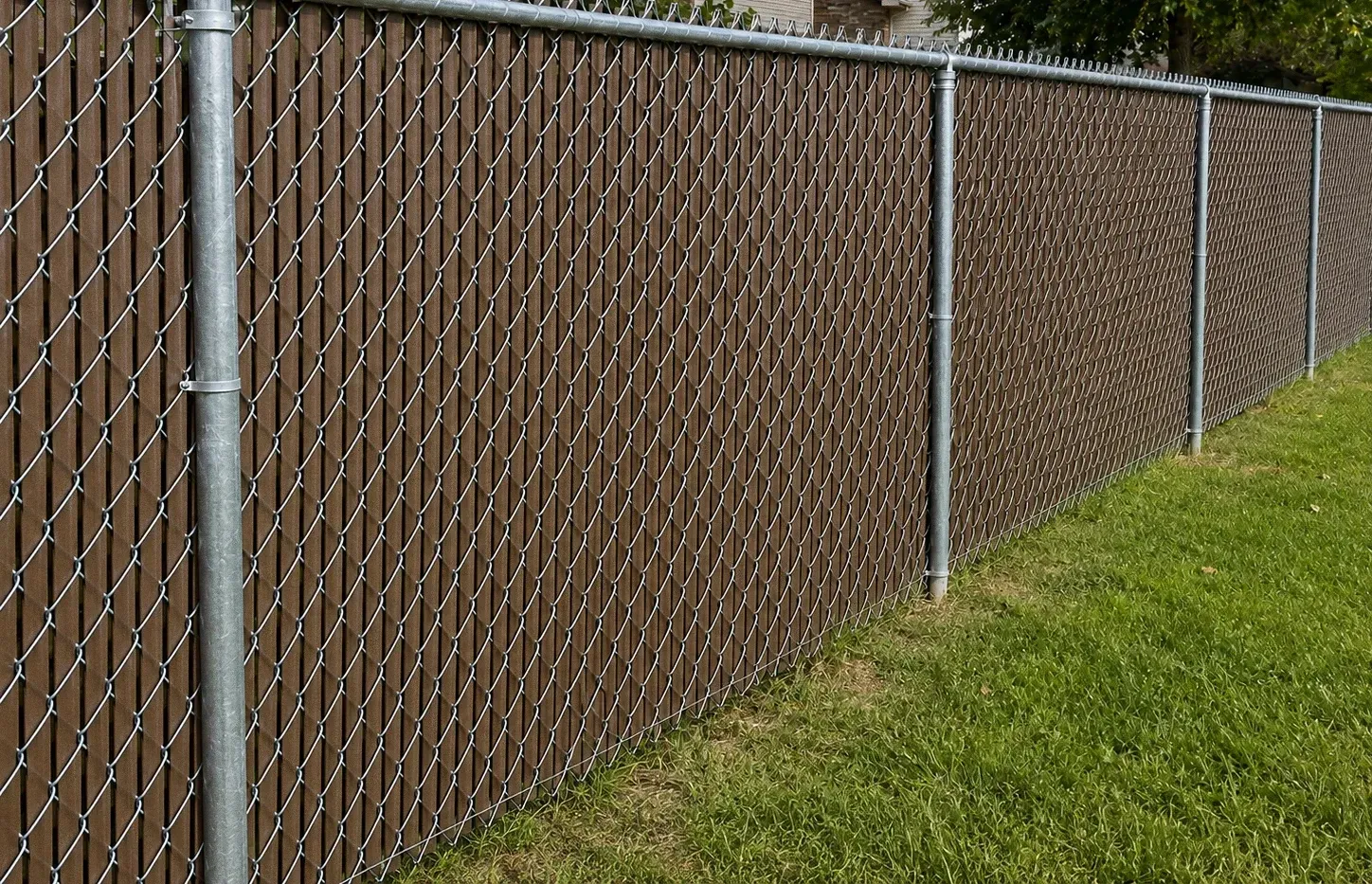 Chain-link fence with brown privacy slats beside a grassy lawn