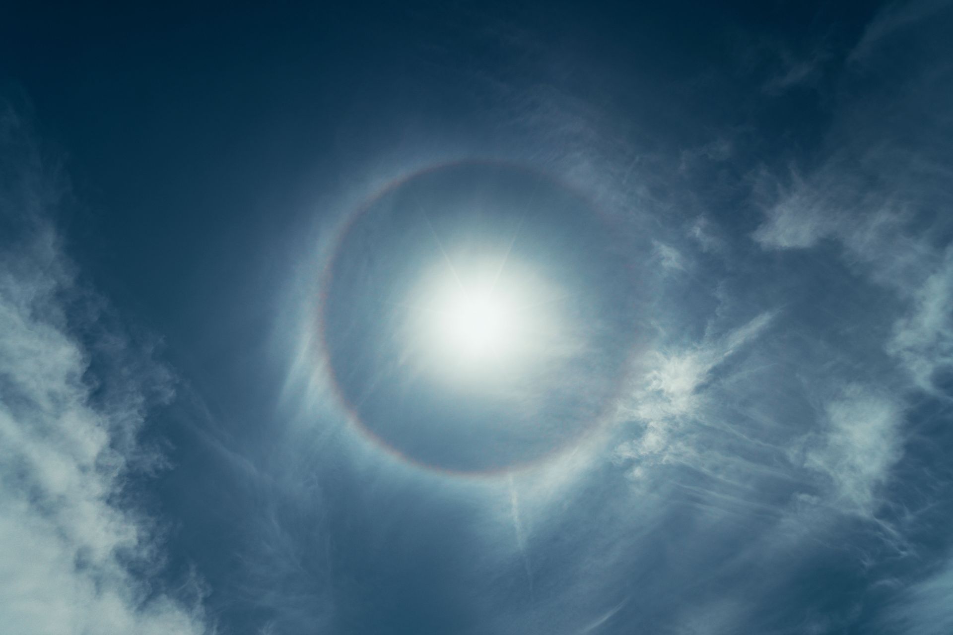 Bright sun behind thin clouds in a blue sky, with a circular halo around it