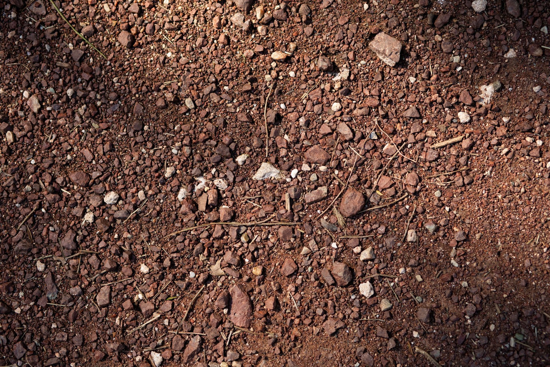 Close-up of reddish-brown gravel and dirt with small stones and shadows.