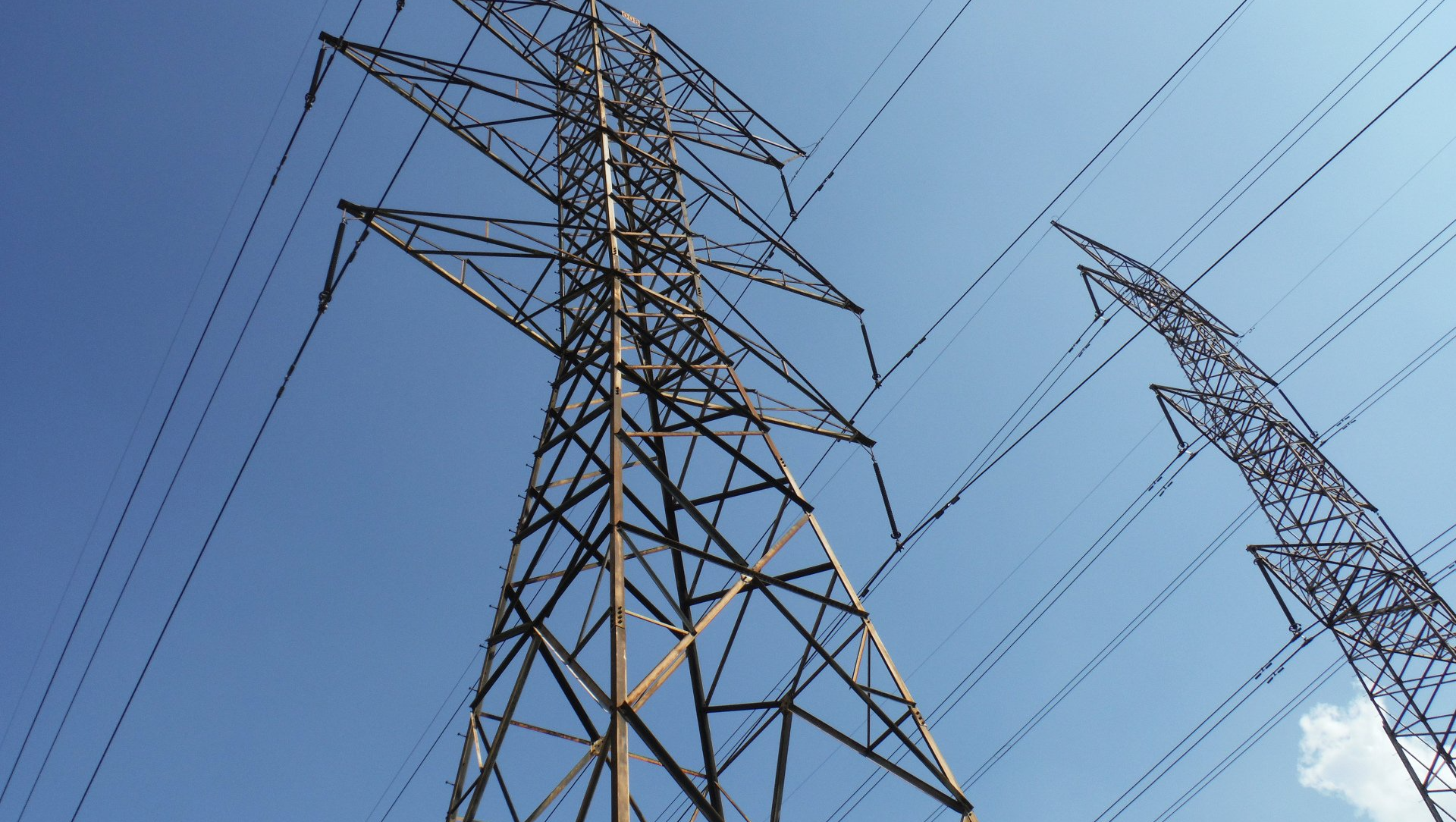 Two tall metal electrical towers against a bright blue sky, supporting multiple power lines.