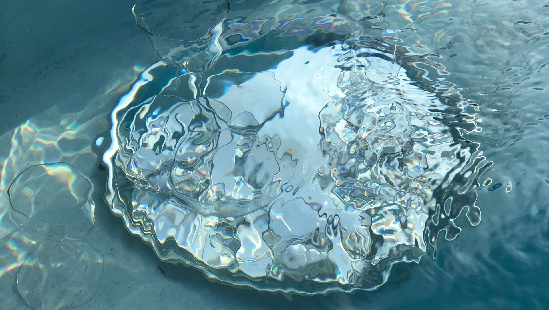 Water splashing on a surface, creating a circular ripple effect with light reflections and a clear blue/silver color palette.