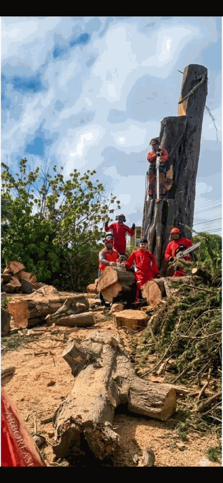 Personas con camisetas rojas subiendo por un sendero rocoso junto a un alto pilar de piedra tallada bajo un cielo nublado