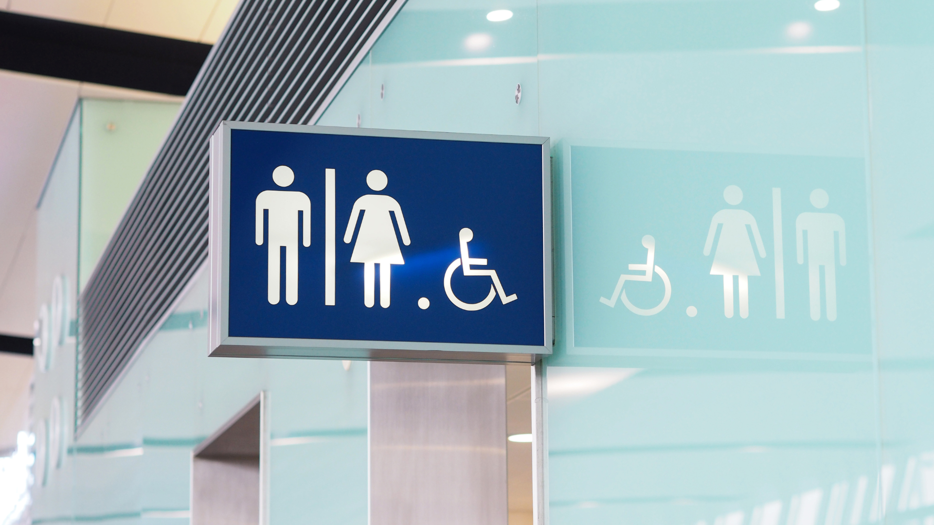 A blue sign for a handicapped toilet is hanging on a glass wall.