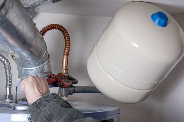 A person is fixing a water heater with a wrench.