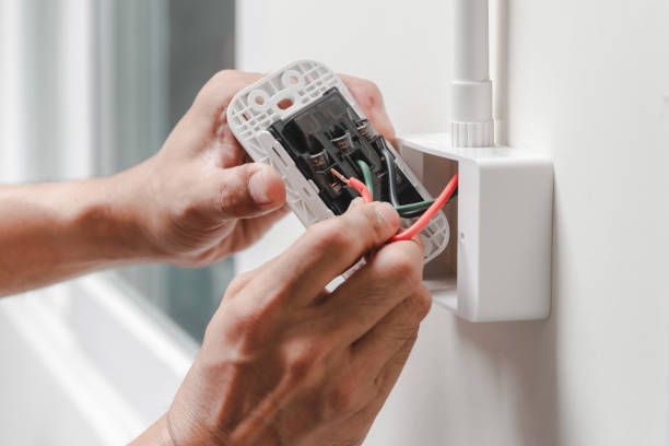 Person wiring an electrical outlet; hands holding wires, white wall and box visible.