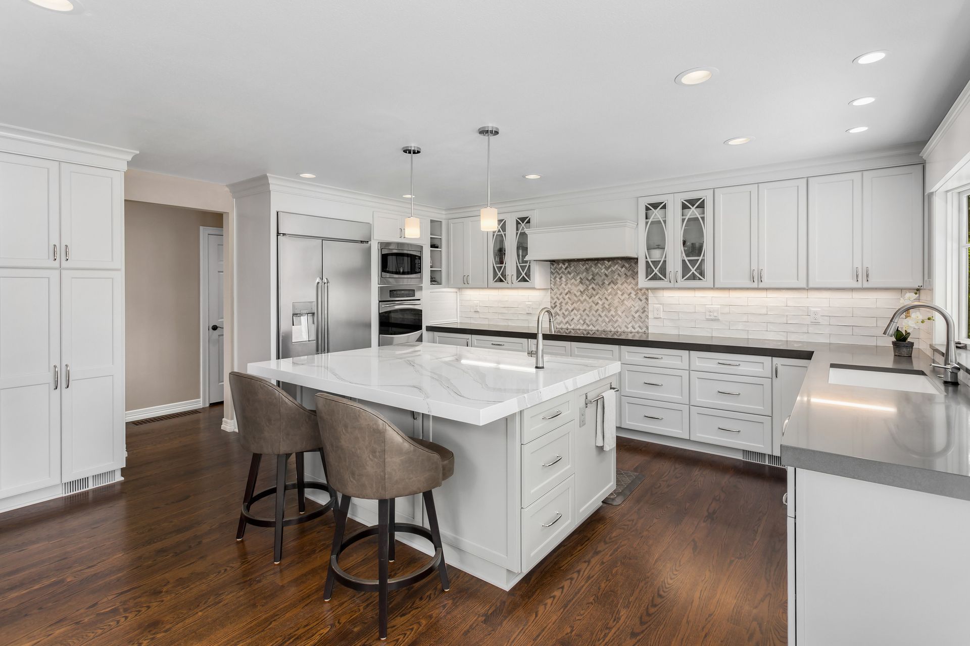 Bright kitchen with white cabinets, island, stainless steel appliances, and dark wood floors.