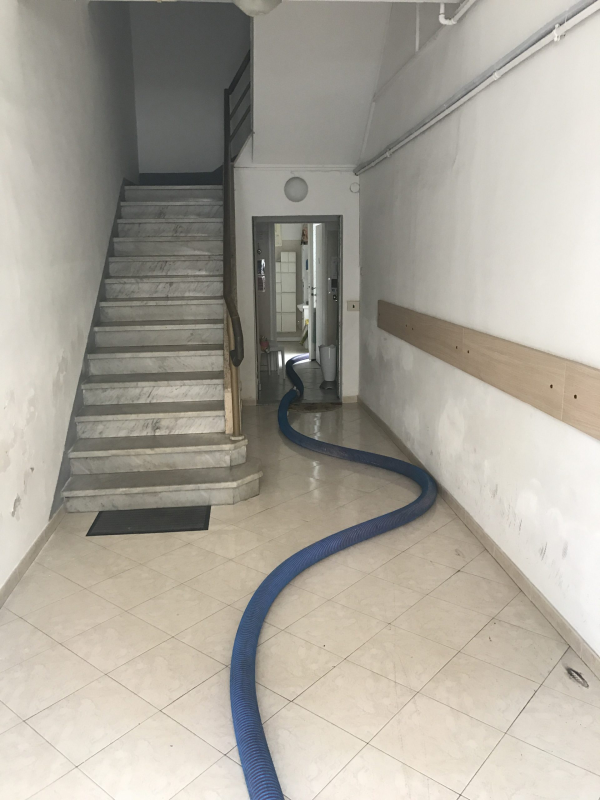 Vano scale interno con un lungo tubo flessibile blu che attraversa il pavimento piastrellato e passa attraverso una porta.