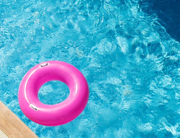 Pink inflatable ring floating in bright blue pool water near the deck edge