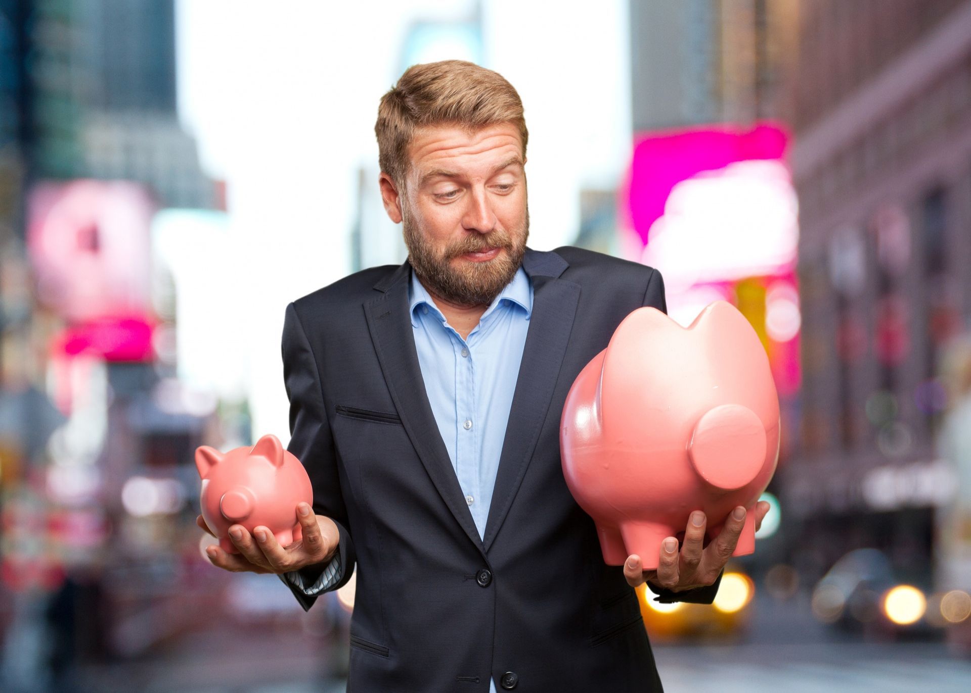 Man in a suit holding two pink piggy banks on a city street