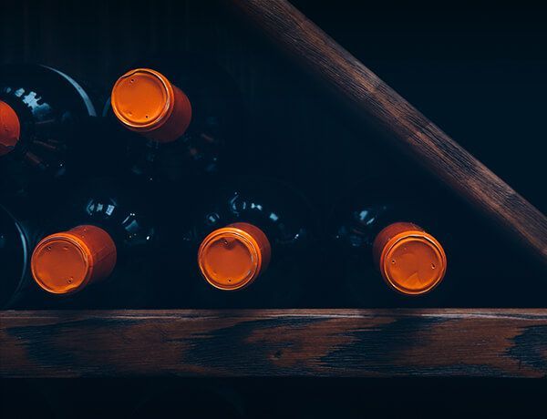 Orange-capped bottles stored in a dark wooden wine rack