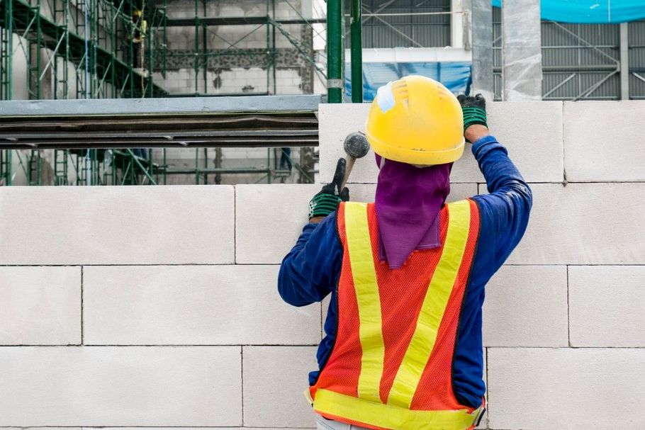 Construction worker in yellow hard hat and safety vest laying white blocks on a wall