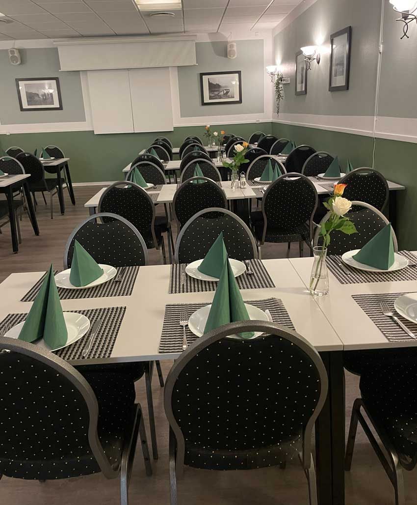 Spisestue med borde, sorte stole og grønne servietter i en stille restaurant