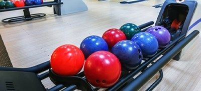 Bowlingkuglereturstativ med røde, blå og lilla kugler på et baneområde