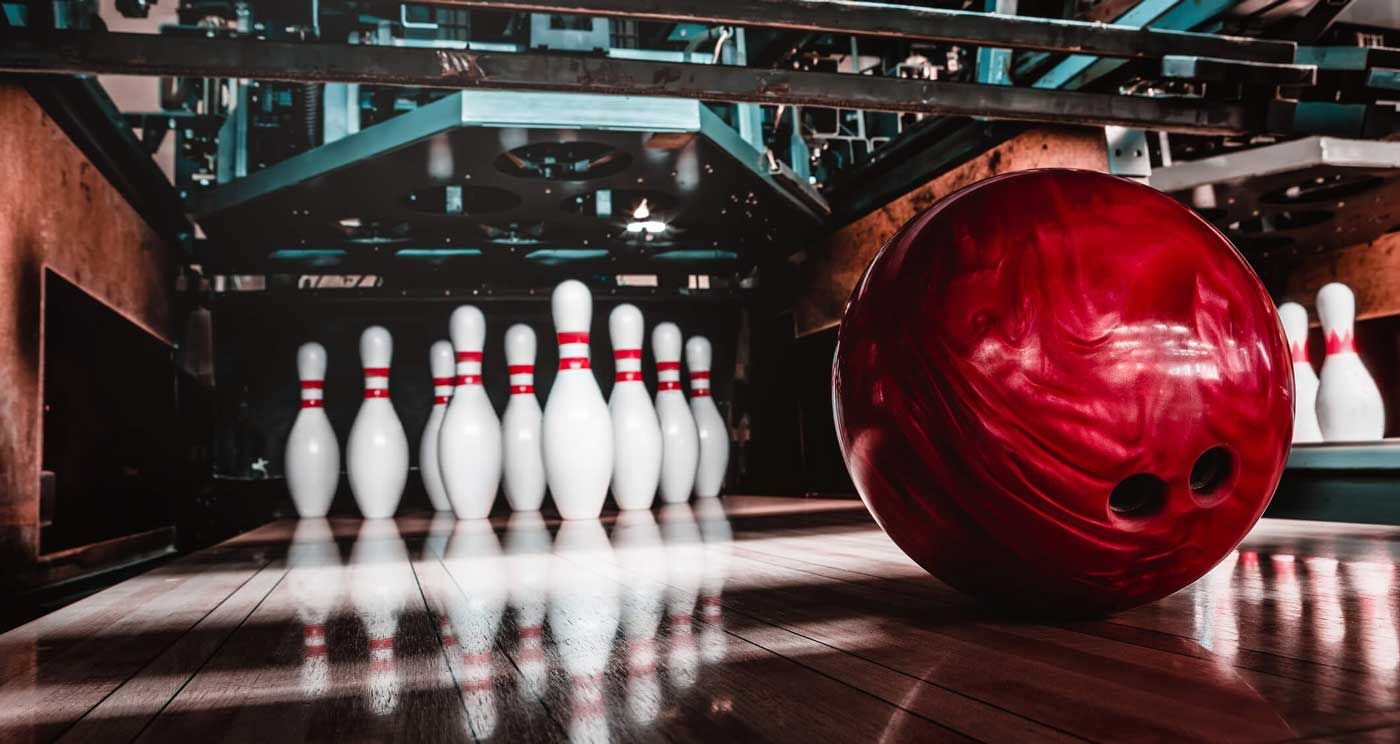 En rød bowlingkugle ruller mod hvide kegler i en bowlingbane.