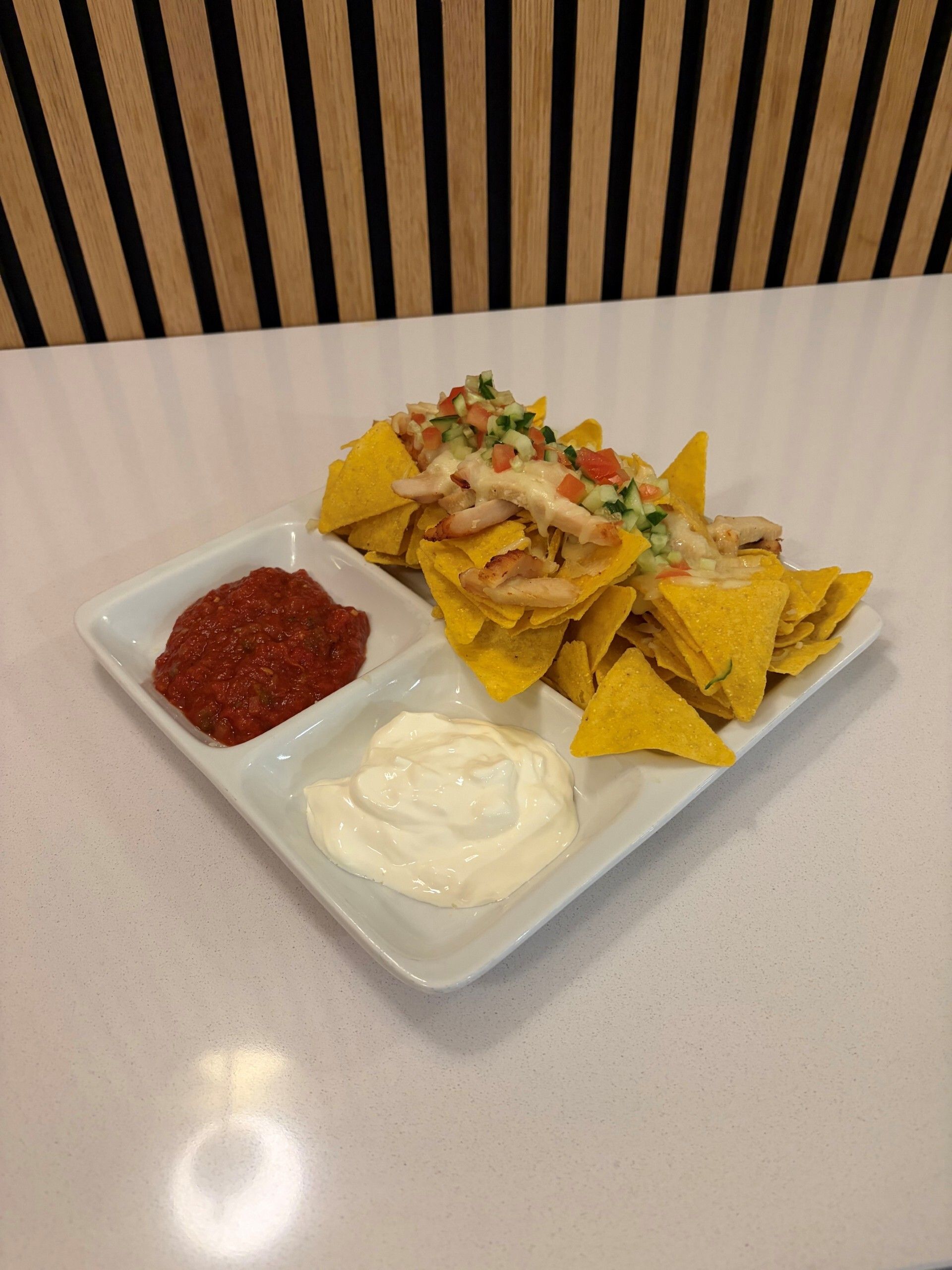 Nachos toppet med cremet sauce, tomater og jalapeños, serveret med salsa og creme fraiche på en hvid tallerken.