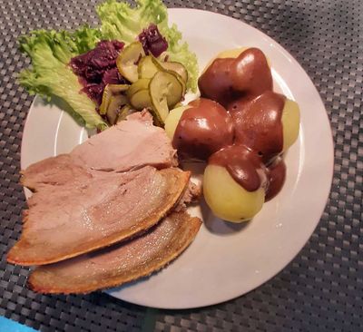 Tallerken med skiver af kød, kartofler i brun sovs og salat på et bord.